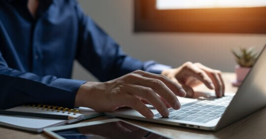 A person holding a smartphone in one hand while working on a laptop, representing managing a PeekYou opt out request online.