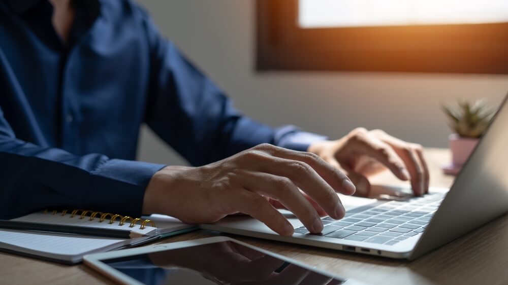 A person holding a smartphone in one hand while working on a laptop, representing managing a PeekYou opt out request online.