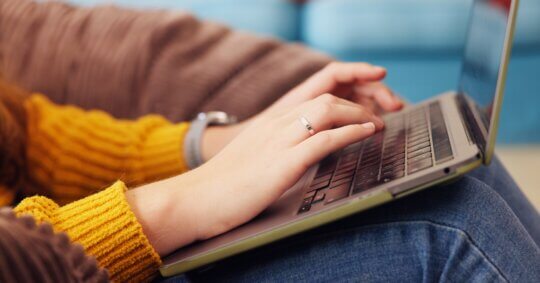 Close-up of a person typing on a laptop keyboard while researching how to opt out of PeopleFinders.