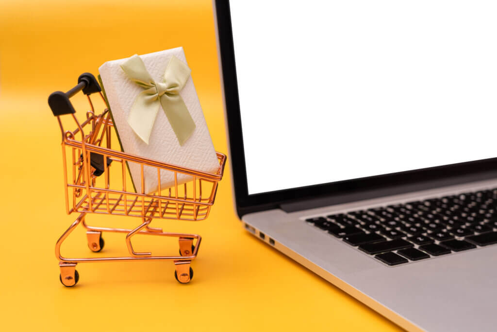 A small shopping cart with a box in it next to a laptop.